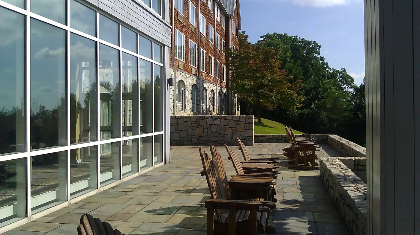 Wooden Adirondack chairs in a row on a stone terrace facing out over a low fieldstone wall in late sun