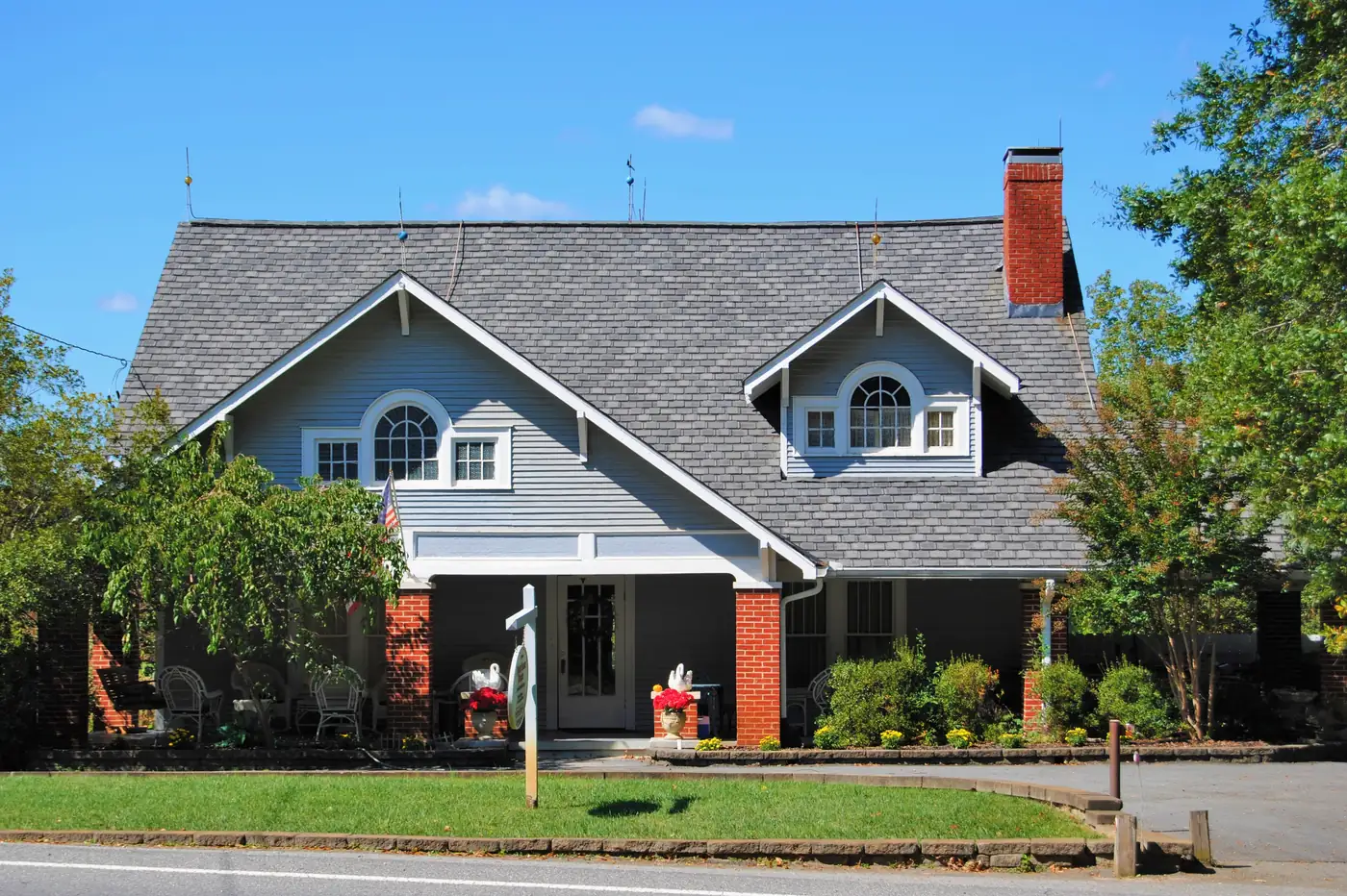 A one-and-a-half-storey Craftsman bungalow with grey-blue siding, two dormers and a full-width porch on brick piers