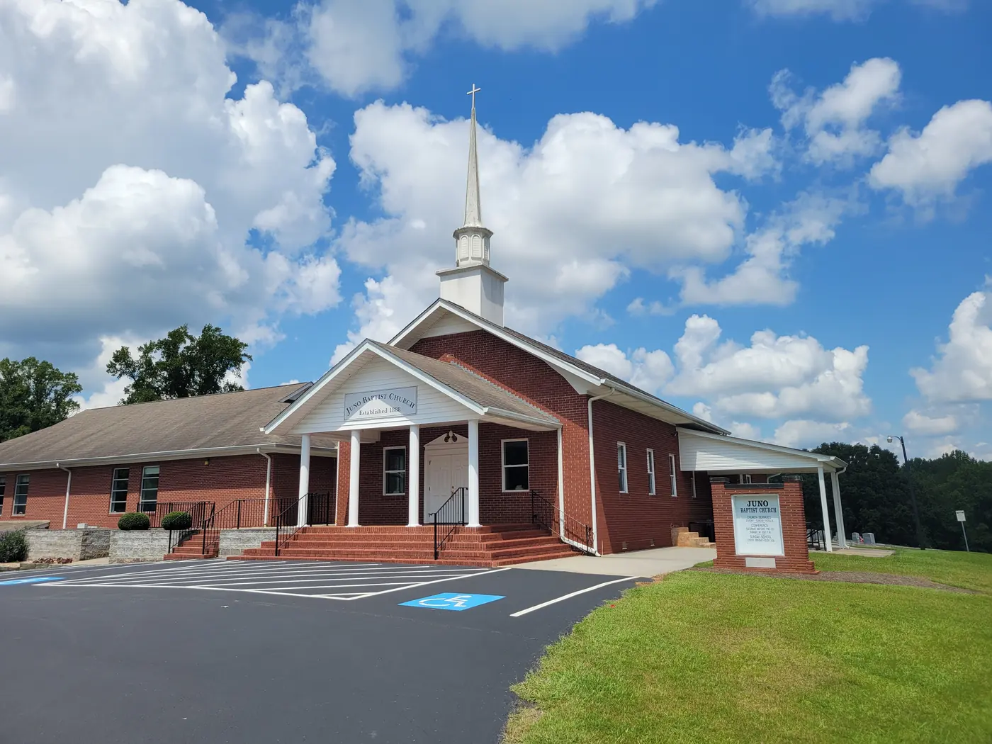A red-brick church with a white columned portico and steeple under a blue sky with large clouds