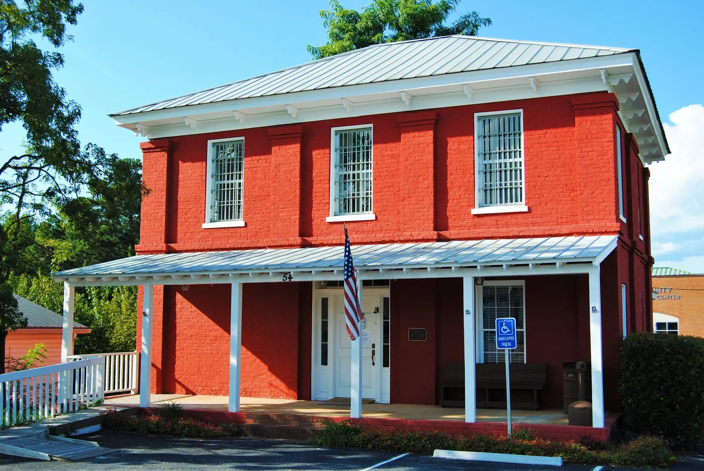 A two-storey red brick building with barred upper windows, a metal hip roof and a white-posted front porch