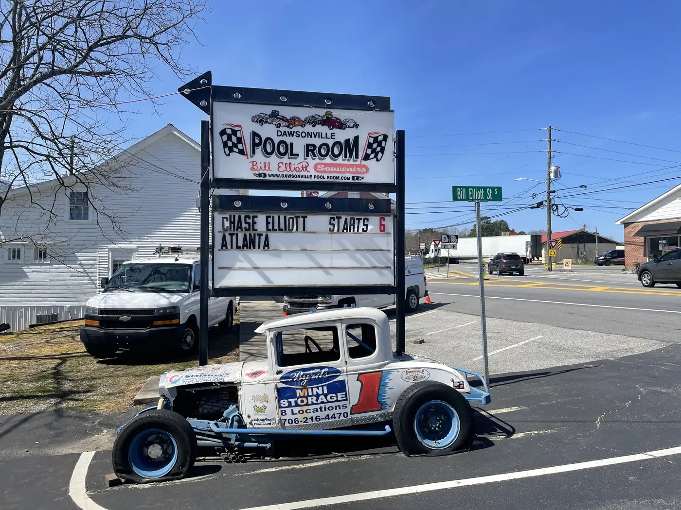 A tall sign reading Dawsonville Pool Room with checkered flags, above an old white number 1 race car