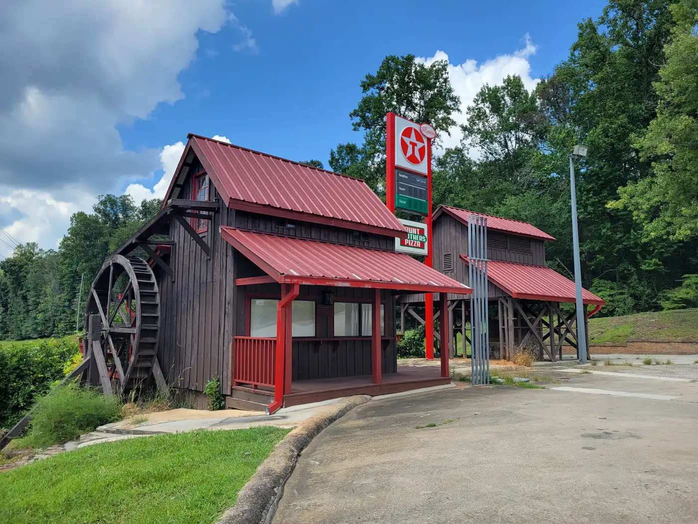 A dark board-and-batten mill with a wooden water wheel and red metal roofs, with wooded hills behind