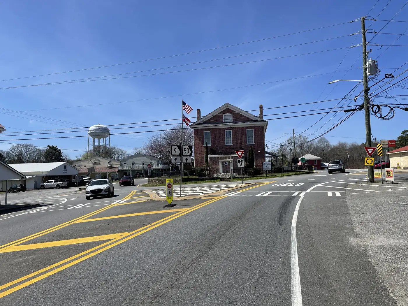 A street leading to a roundabout around a red-brick courthouse, with route shields, flags and a white water tower behind